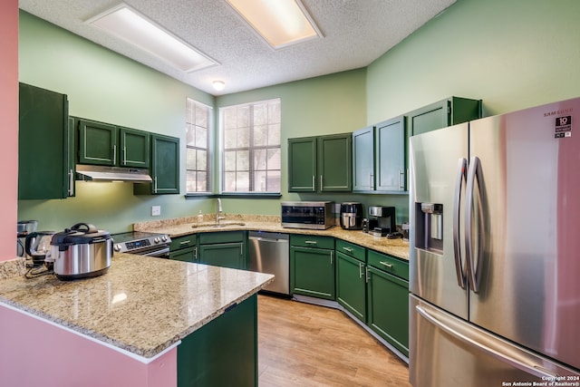 kitchen featuring appliances with stainless steel finishes, green cabinets, kitchen peninsula, sink, and light wood-type flooring