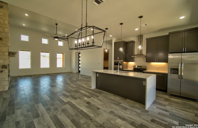 kitchen featuring wall chimney exhaust hood, dark hardwood / wood-style flooring, pendant lighting, stainless steel appliances, and a center island with sink