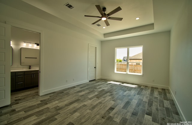 unfurnished bedroom with connected bathroom, a tray ceiling, hardwood / wood-style floors, and ceiling fan