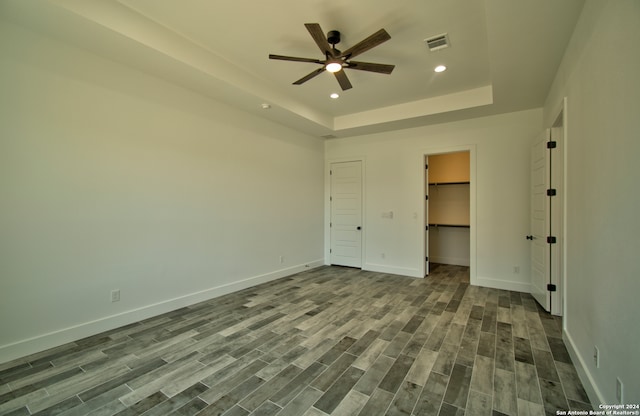 unfurnished bedroom with a spacious closet, ceiling fan, a raised ceiling, and hardwood / wood-style flooring