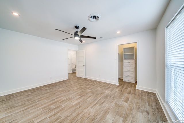 unfurnished bedroom with a closet, a walk in closet, ceiling fan, and light hardwood / wood-style floors