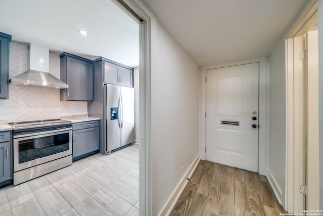 kitchen with light hardwood / wood-style flooring, backsplash, light stone countertops, wall chimney exhaust hood, and appliances with stainless steel finishes