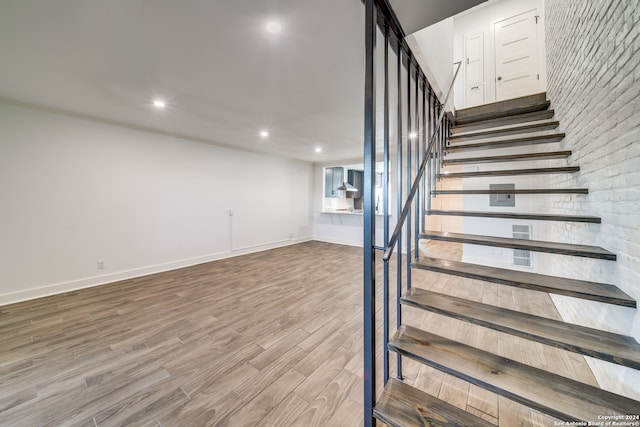 stairway with brick wall and hardwood / wood-style flooring