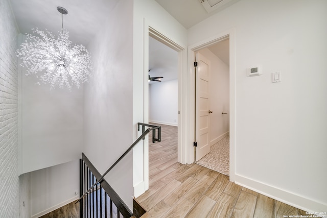 hallway featuring light wood-type flooring, a chandelier, and brick wall