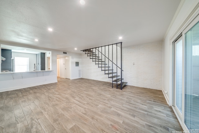 unfurnished living room featuring a textured ceiling, brick wall, crown molding, and light hardwood / wood-style flooring