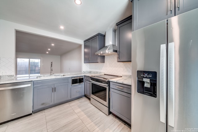 kitchen featuring light stone counters, sink, appliances with stainless steel finishes, gray cabinetry, and wall chimney range hood