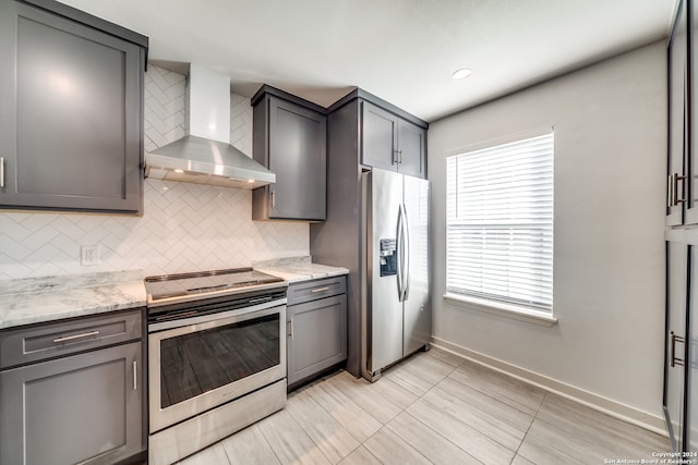 kitchen with stainless steel appliances, light stone counters, gray cabinets, and wall chimney range hood