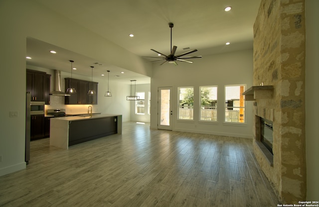 living room with sink, a fireplace, light hardwood / wood-style flooring, a towering ceiling, and ceiling fan