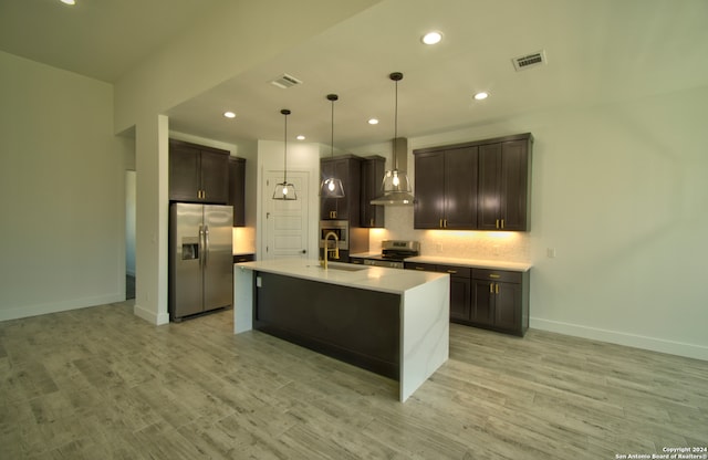 kitchen with light wood-type flooring, hanging light fixtures, wall chimney range hood, stainless steel appliances, and dark brown cabinetry