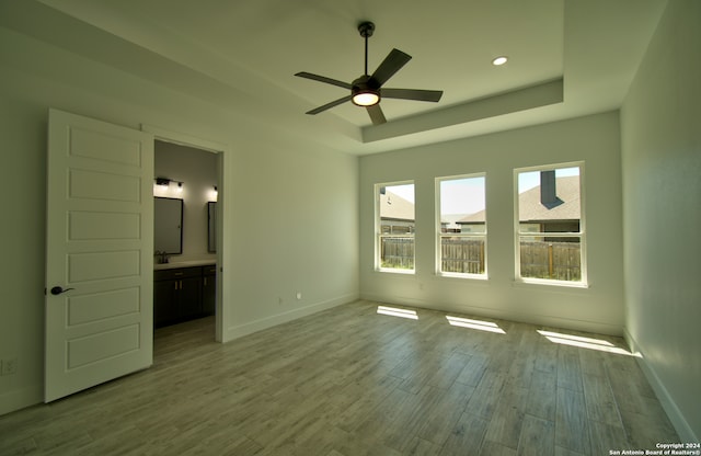 unfurnished bedroom with connected bathroom, a tray ceiling, ceiling fan, and light hardwood / wood-style flooring