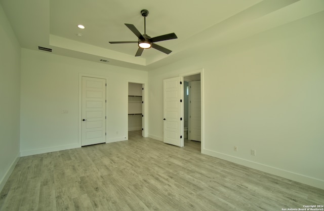 unfurnished bedroom featuring light wood-type flooring, a tray ceiling, and ceiling fan