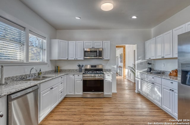 kitchen with appliances with stainless steel finishes, light hardwood / wood-style flooring, sink, and white cabinets