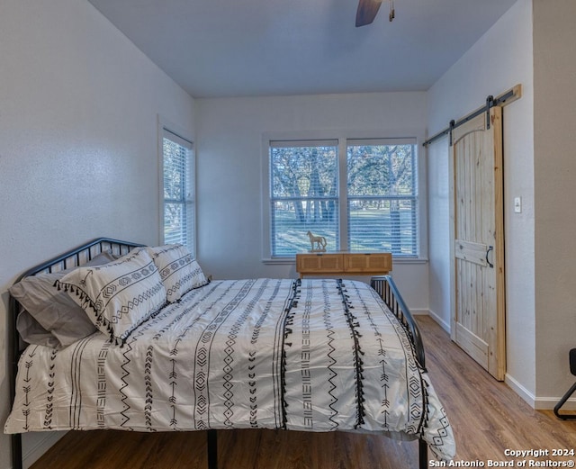 bedroom with hardwood / wood-style floors, ceiling fan, and a barn door