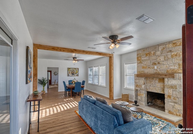 living room featuring a textured ceiling, wood-type flooring, ceiling fan, and a stone fireplace