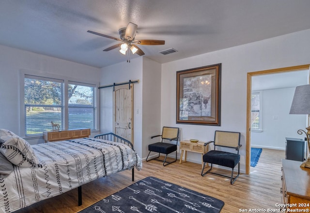 bedroom with a barn door, ceiling fan, and hardwood / wood-style flooring