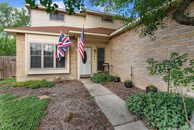 view of exterior entry with fence and brick siding