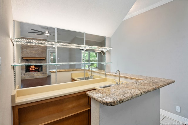 kitchen with crown molding, a brick fireplace, sink, ceiling fan, and vaulted ceiling