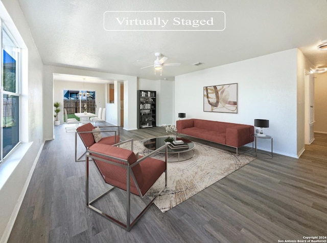 living room featuring ceiling fan with notable chandelier, wood finished floors, and baseboards