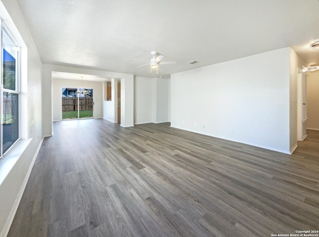 unfurnished living room with dark wood-type flooring, ceiling fan with notable chandelier, baseboards, and a textured ceiling