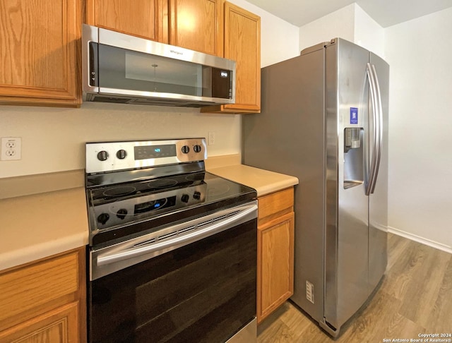 kitchen featuring light countertops, light wood-type flooring, appliances with stainless steel finishes, and brown cabinets