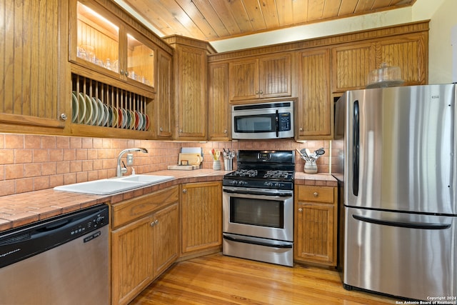 kitchen featuring appliances with stainless steel finishes, light hardwood / wood-style floors, tile counters, wood ceiling, and sink