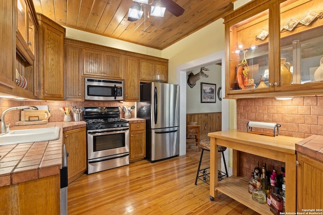 kitchen with a sink, tile countertops, appliances with stainless steel finishes, wooden ceiling, and wainscoting