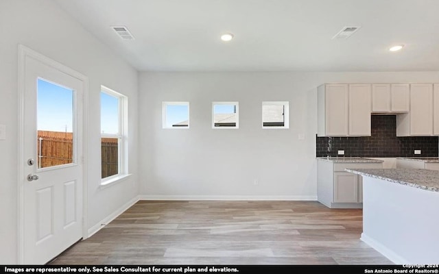 kitchen with light stone counters, light wood-type flooring, white cabinetry, and decorative backsplash