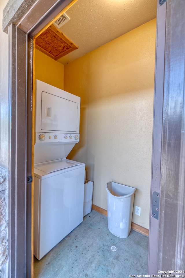 clothes washing area with a textured ceiling and stacked washer and clothes dryer