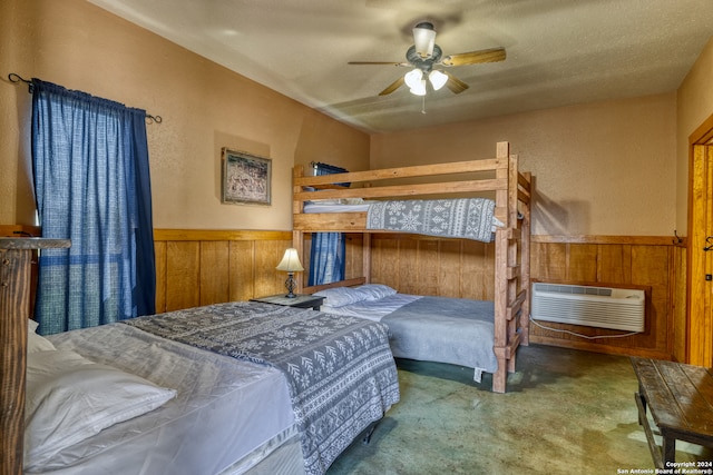 bedroom with a wall unit AC, a textured ceiling, wood walls, ceiling fan, and carpet flooring