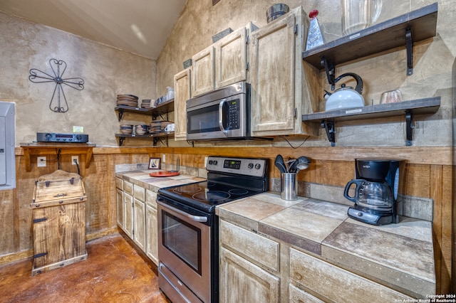 kitchen featuring concrete floors, vaulted ceiling, tile countertops, electric panel, and stainless steel appliances