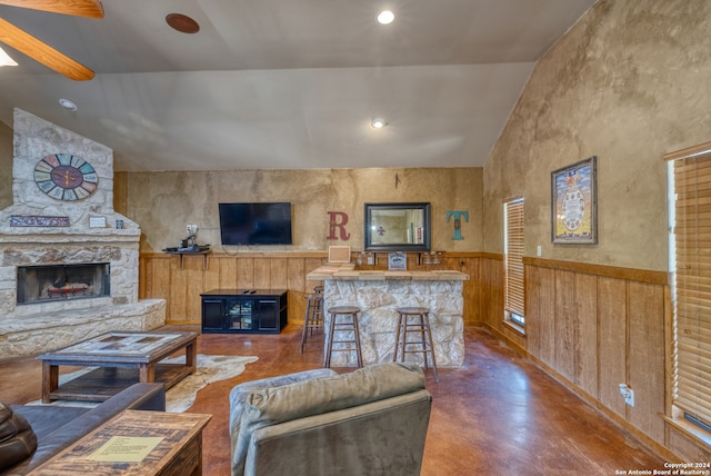 living room featuring ceiling fan, a stone fireplace, high vaulted ceiling, and concrete flooring