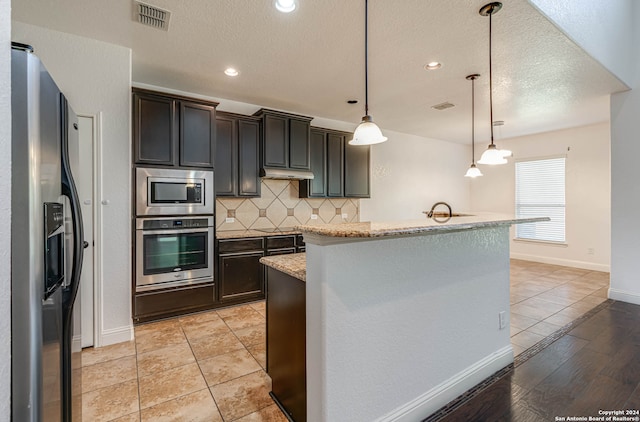 kitchen featuring decorative light fixtures, tasteful backsplash, light hardwood / wood-style floors, stainless steel appliances, and light stone counters