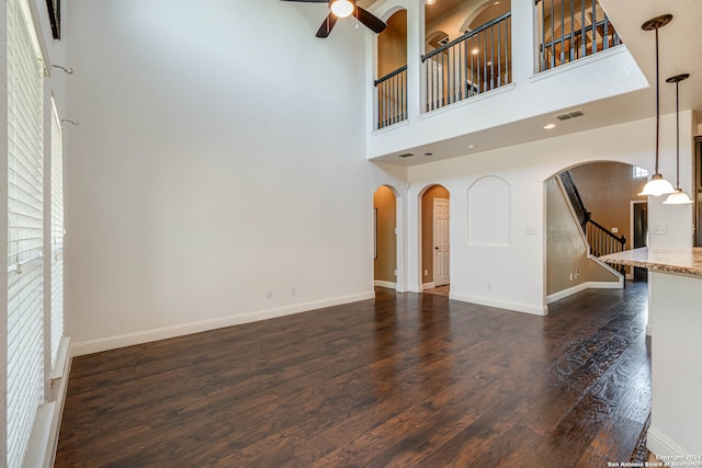 unfurnished living room with a high ceiling, ceiling fan, and dark hardwood / wood-style flooring