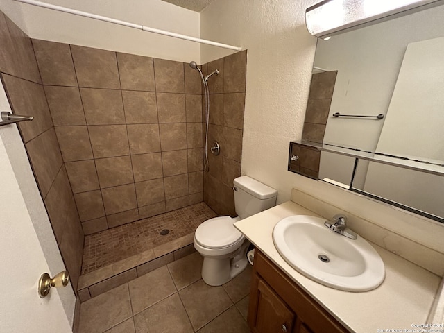 bathroom with vanity, toilet, a tile shower, and tile patterned flooring