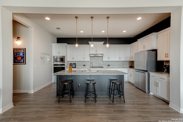 kitchen featuring a breakfast bar area, appliances with stainless steel finishes, white cabinetry, and light hardwood / wood-style floors