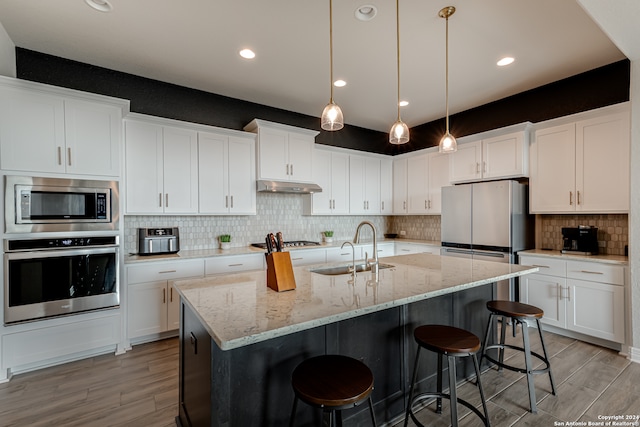 kitchen featuring light wood-type flooring, white cabinets, appliances with stainless steel finishes, and a center island with sink