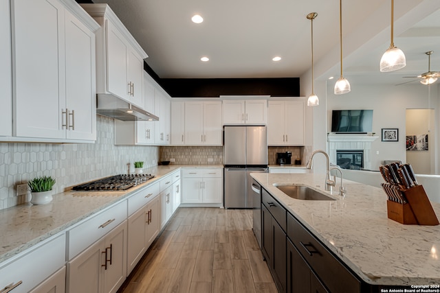 kitchen featuring stainless steel appliances, sink, light stone counters, light wood-type flooring, and white cabinets