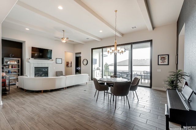 dining room featuring ceiling fan with notable chandelier, a fireplace, beamed ceiling, and wood-type flooring