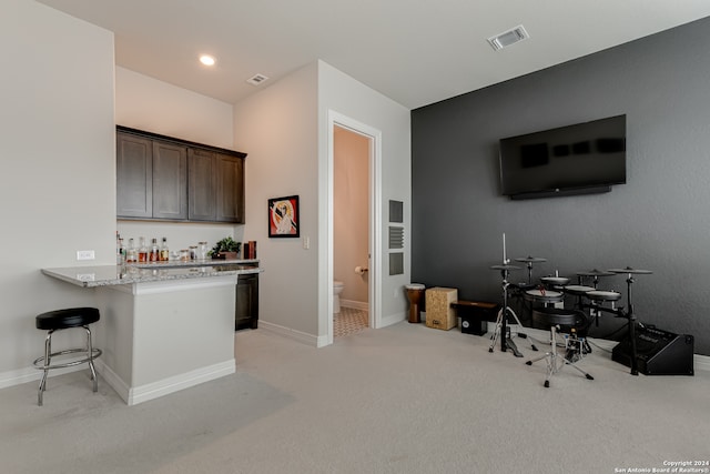 kitchen featuring a breakfast bar area, light carpet, dark brown cabinets, and light stone countertops