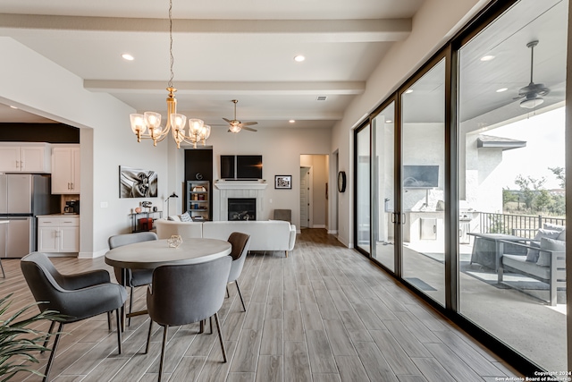 dining space with ceiling fan with notable chandelier, a fireplace, light hardwood / wood-style floors, and beamed ceiling