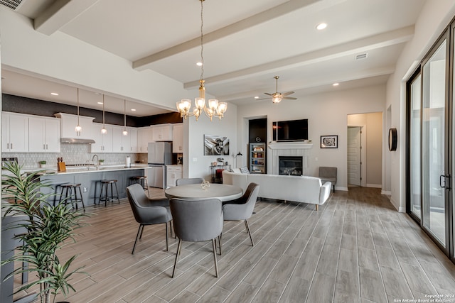 dining area featuring a tiled fireplace, plenty of natural light, beam ceiling, and light hardwood / wood-style floors