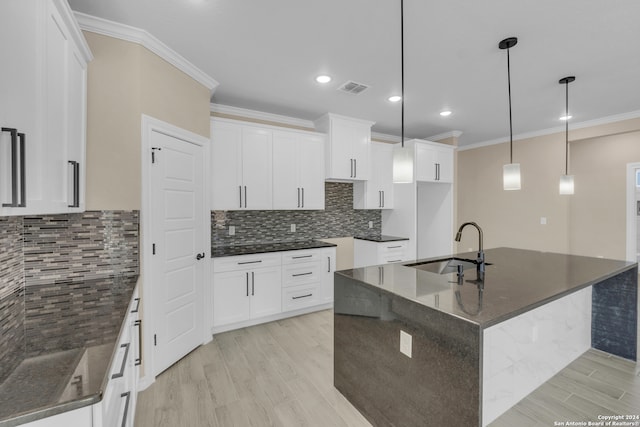 kitchen with a kitchen island with sink, dark stone counters, white cabinetry, decorative light fixtures, and sink