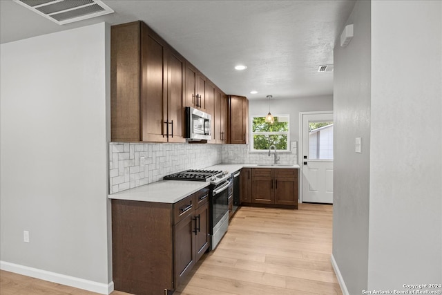 kitchen featuring appliances with stainless steel finishes, backsplash, pendant lighting, light hardwood / wood-style flooring, and sink