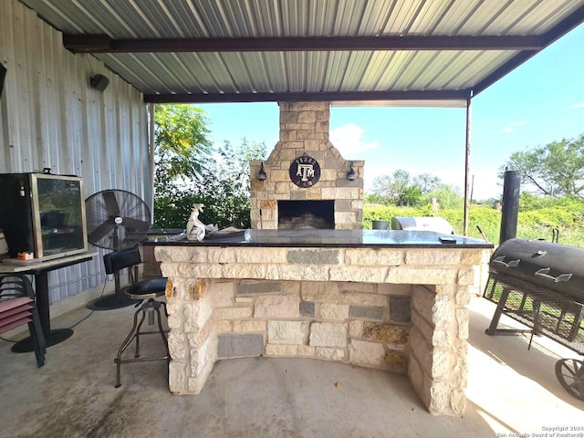 view of patio / terrace featuring exterior bar, an outdoor stone fireplace, and an outdoor kitchen