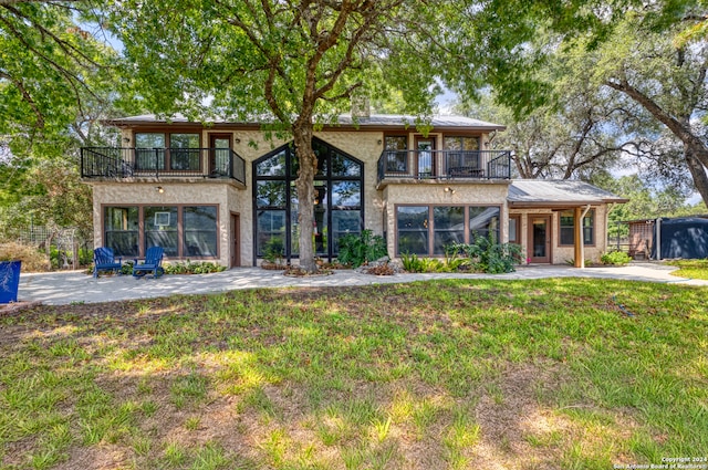 rear view of property featuring a balcony, a patio area, and a lawn