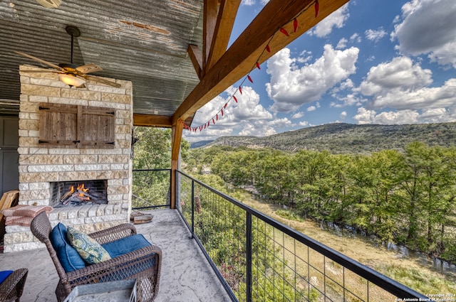 balcony with an outdoor stone fireplace, a mountain view, and ceiling fan