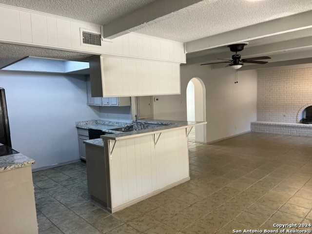 kitchen with a fireplace, black refrigerator, ceiling fan, beam ceiling, and a textured ceiling