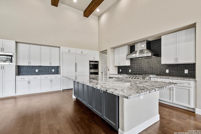 kitchen with an island with sink, a towering ceiling, appliances with stainless steel finishes, and white cabinets