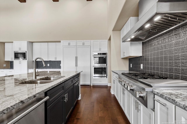 kitchen with dark wood finished floors, built in appliances, exhaust hood, white cabinetry, and a sink