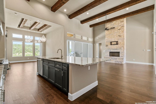 kitchen featuring light stone counters, a sink, a stone fireplace, stainless steel dishwasher, and open floor plan